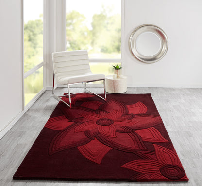 Red floral area rug with oversized petals, white modern lounge chair, circular metal wall art, small plant on beige side table.