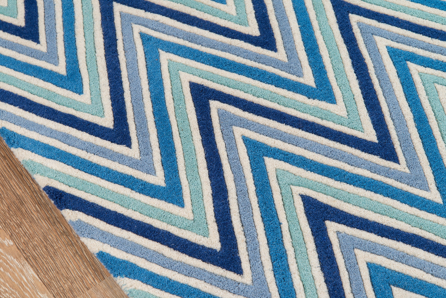 Blue chevron rug with navy, teal & light blue zigzag stripes on a wooden floor edge.