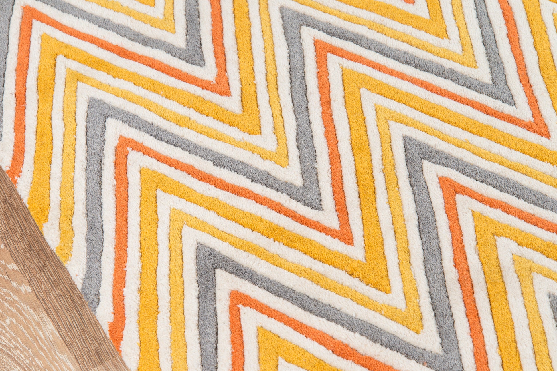 Chevron zigzag rug in orange, yellow and gray on white, retro mid-century style with wood floor edge.