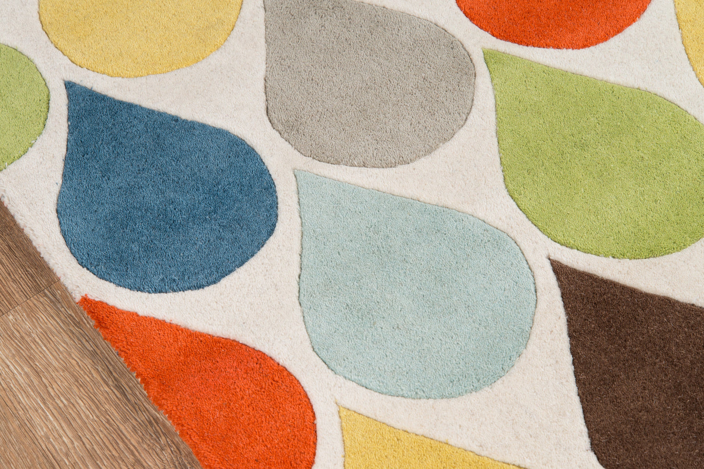 Colorful abstract area rug with multicolored pebble shapes on off-white background, folded corner over wood floor.