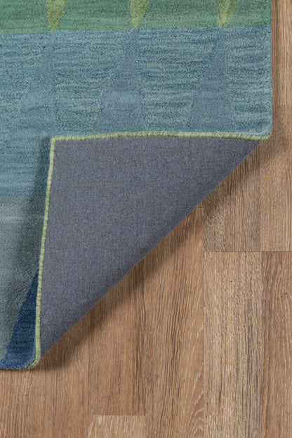 Blue-green geometric rug with lime trim; folded corner reveals gray underside on wooden floor.