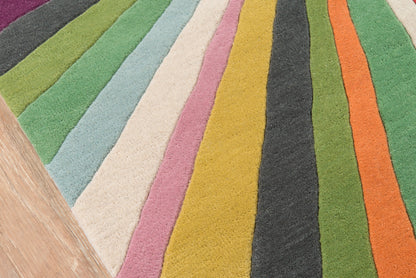 Colorful striped shag rug with rainbow stripes in greens, blues, pinks, yellows, oranges and black; wood edge visible.