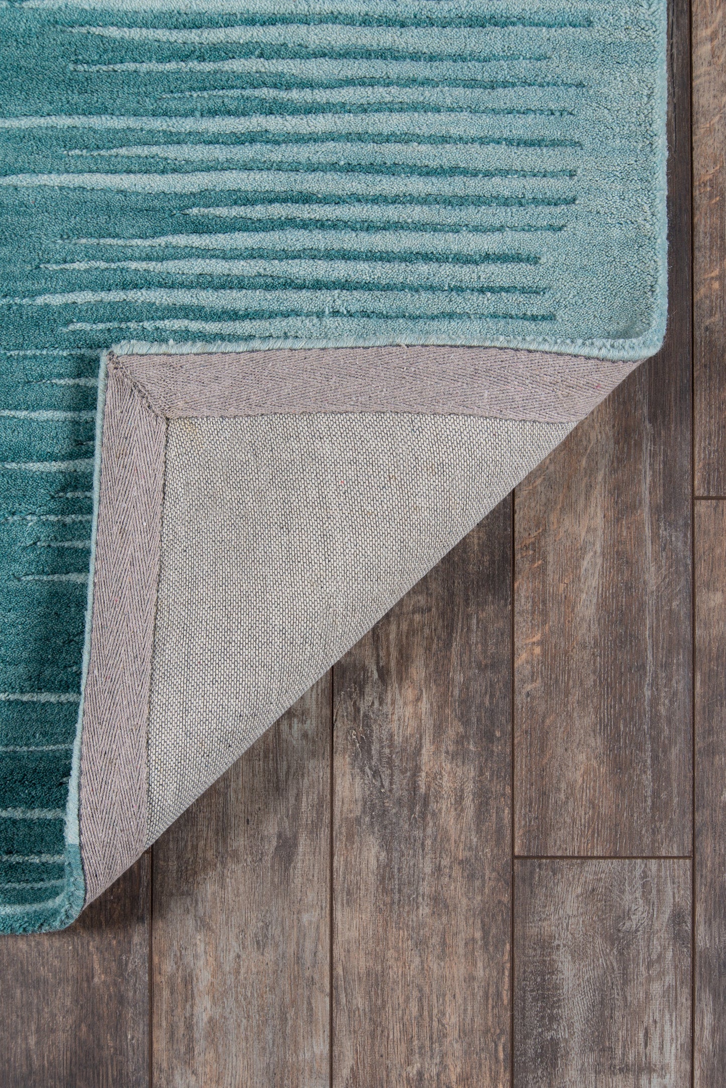 Teal striped area rug with folded corner revealing beige underside on a dark wood floor.