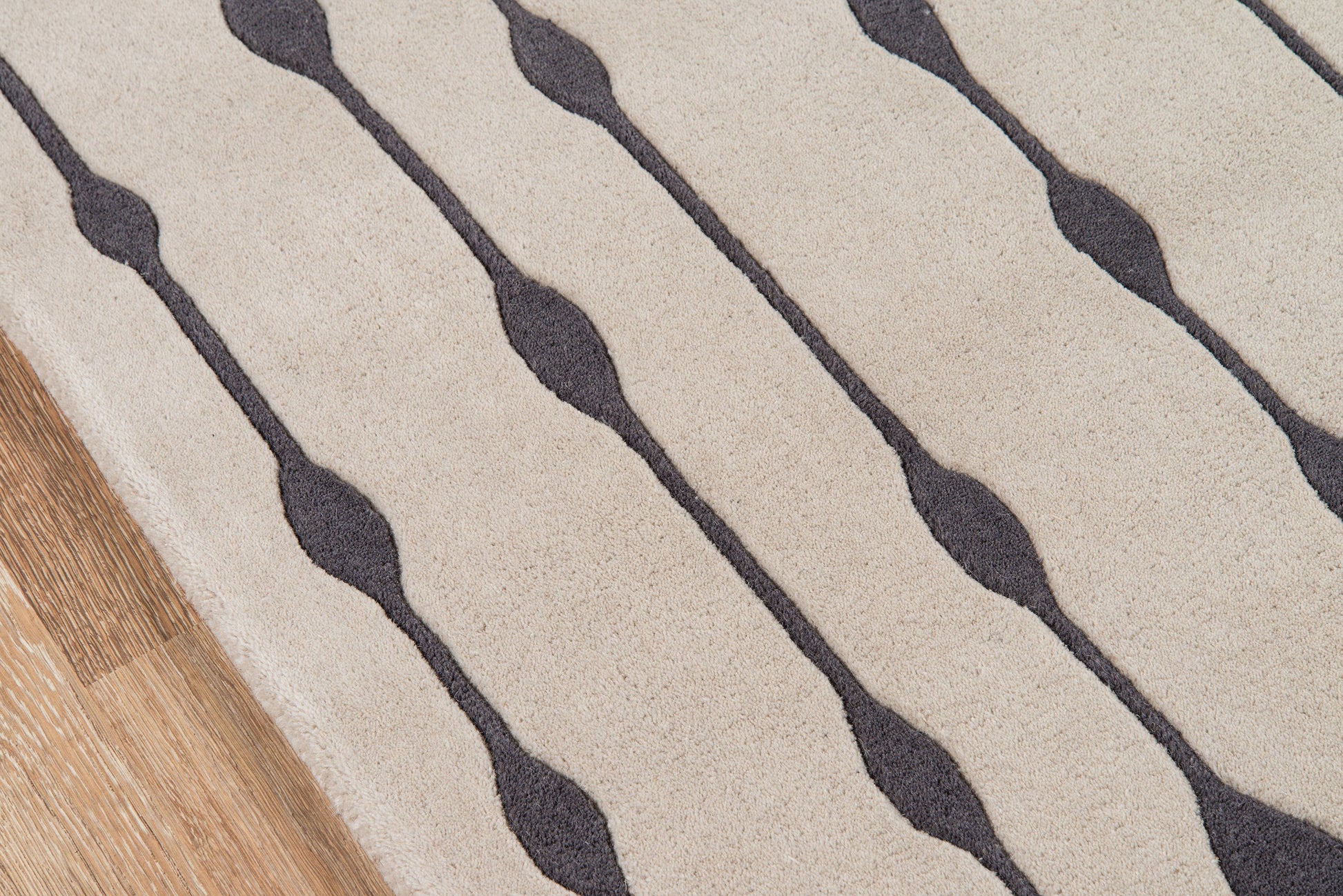 Beige rug with dark gray wavy lines, textured fabric, diagonal stripe pattern & wood floor edge visible.