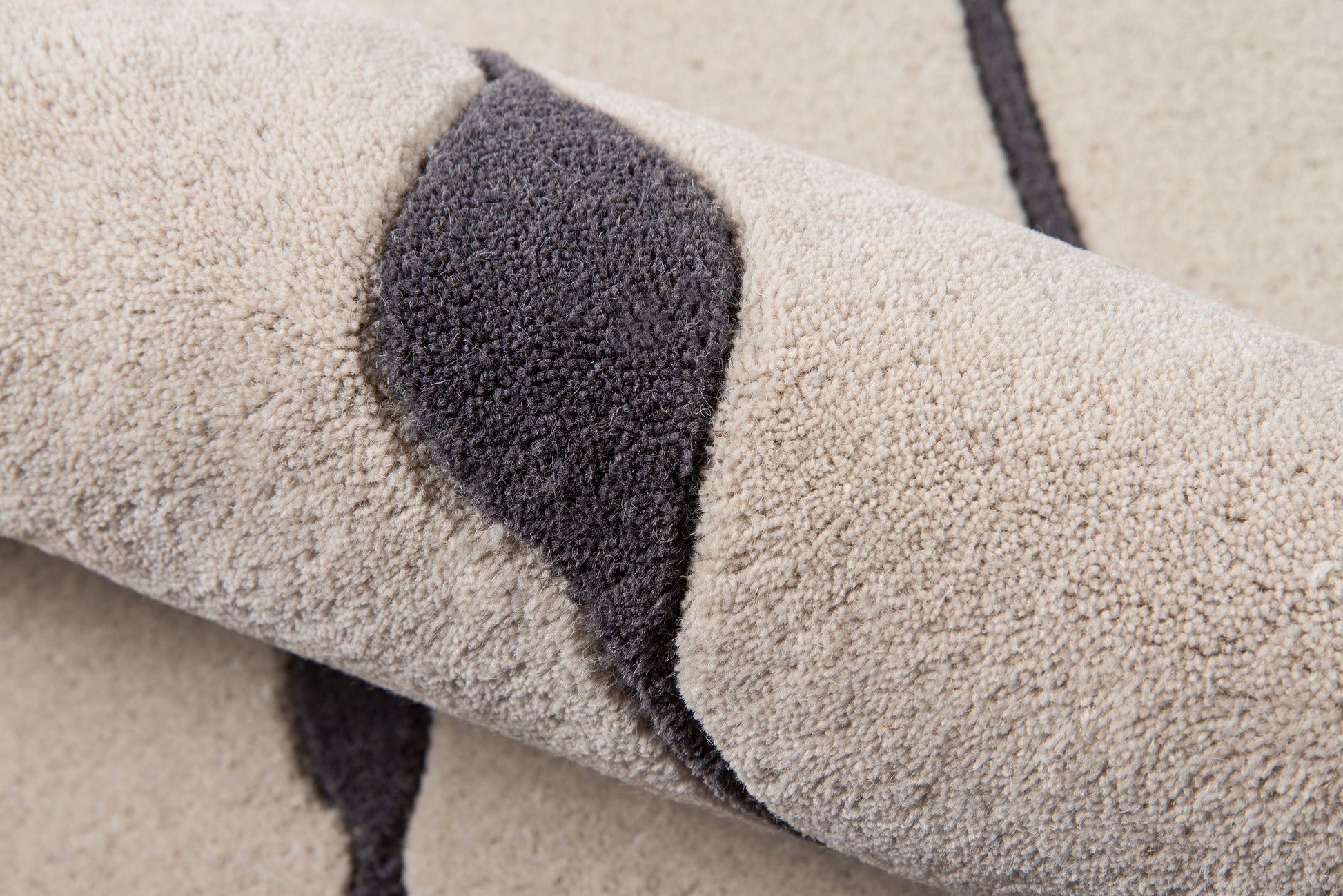Beige plush rug with dark gray curved stripe, high-pile texture, rolled rug.