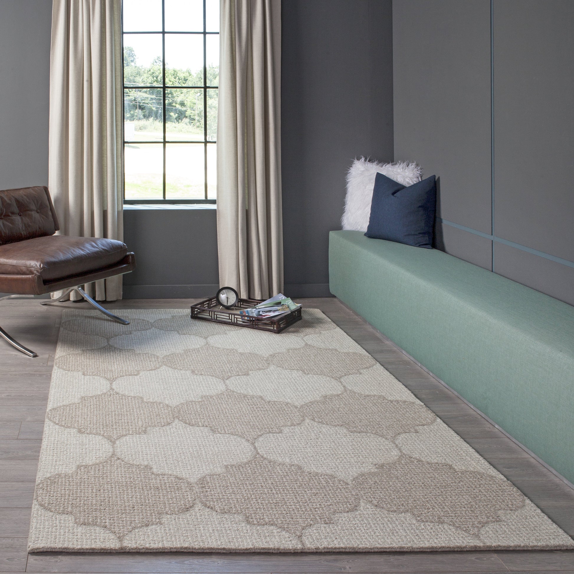 Beige trellis-pattern area rug (4' x 6') in a modern living room with gray walls, a green upholstered bench, and a brown leather chair.