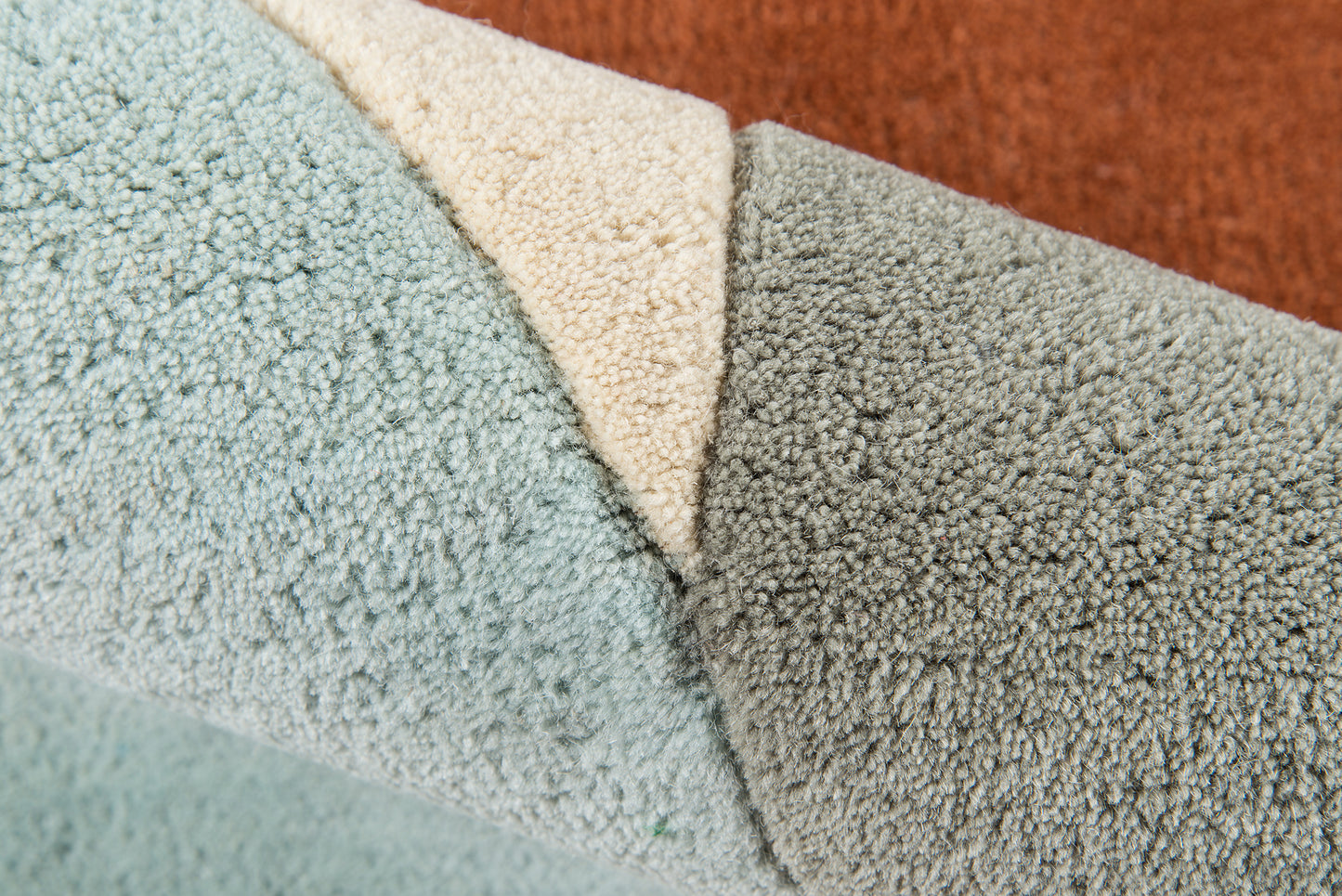 Close-up of plush rug samples in light blue, cream, gray and rust orange with dense looped pile.