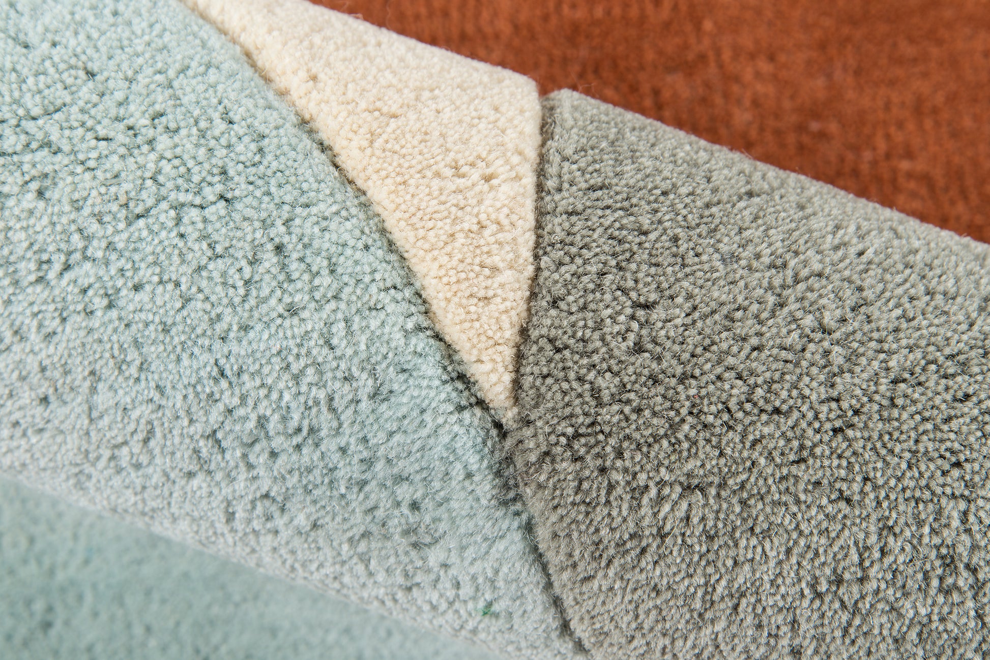 Close-up of plush rug samples in light blue, cream, gray and rust orange with dense looped pile.
