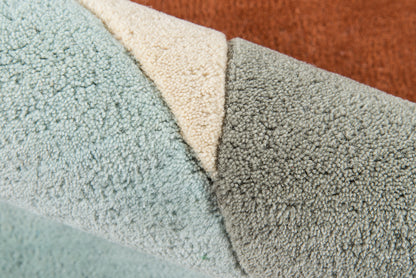 Close-up of plush rug samples in light blue, cream, gray and rust orange with dense looped pile.