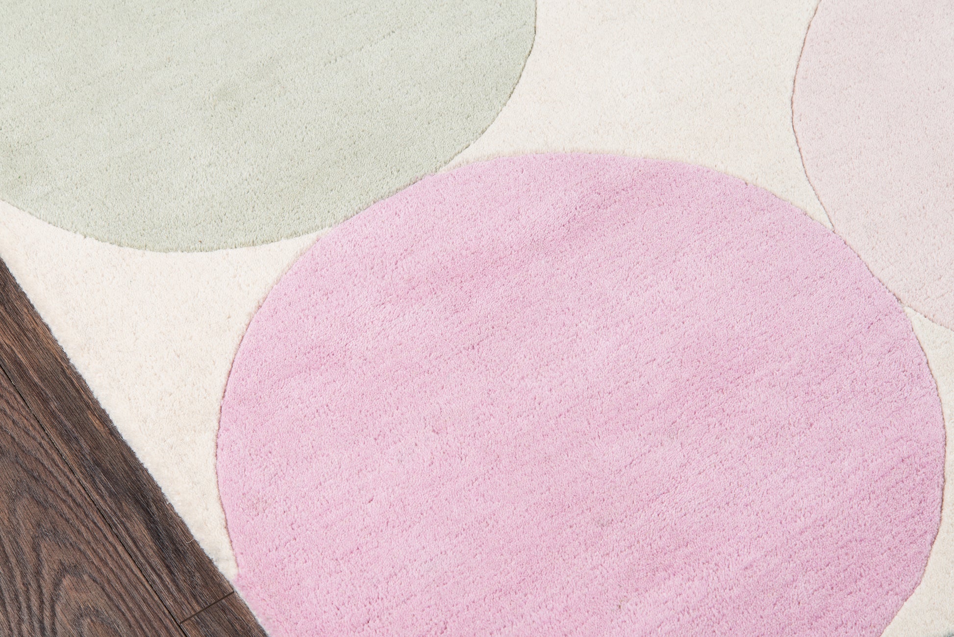Pastel circular rug pattern with sage green, pink, and lavender circles on a cream background; wood floor edge.
