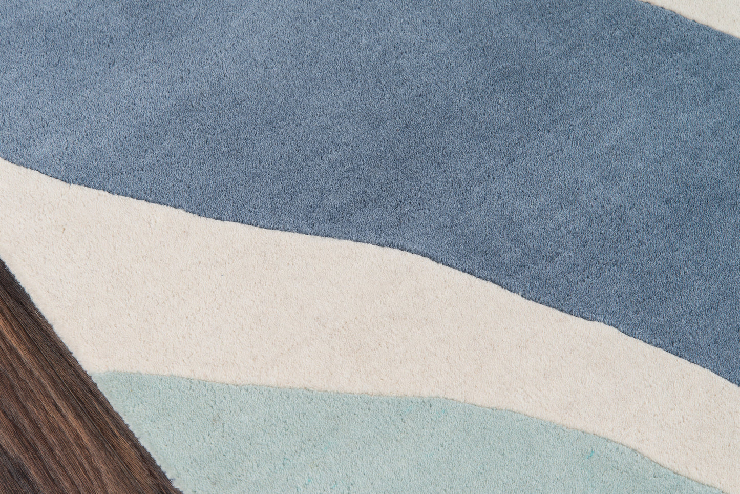 Abstract blue rug with wavy stripes in navy, cream, and pale teal; wooden edge visible.