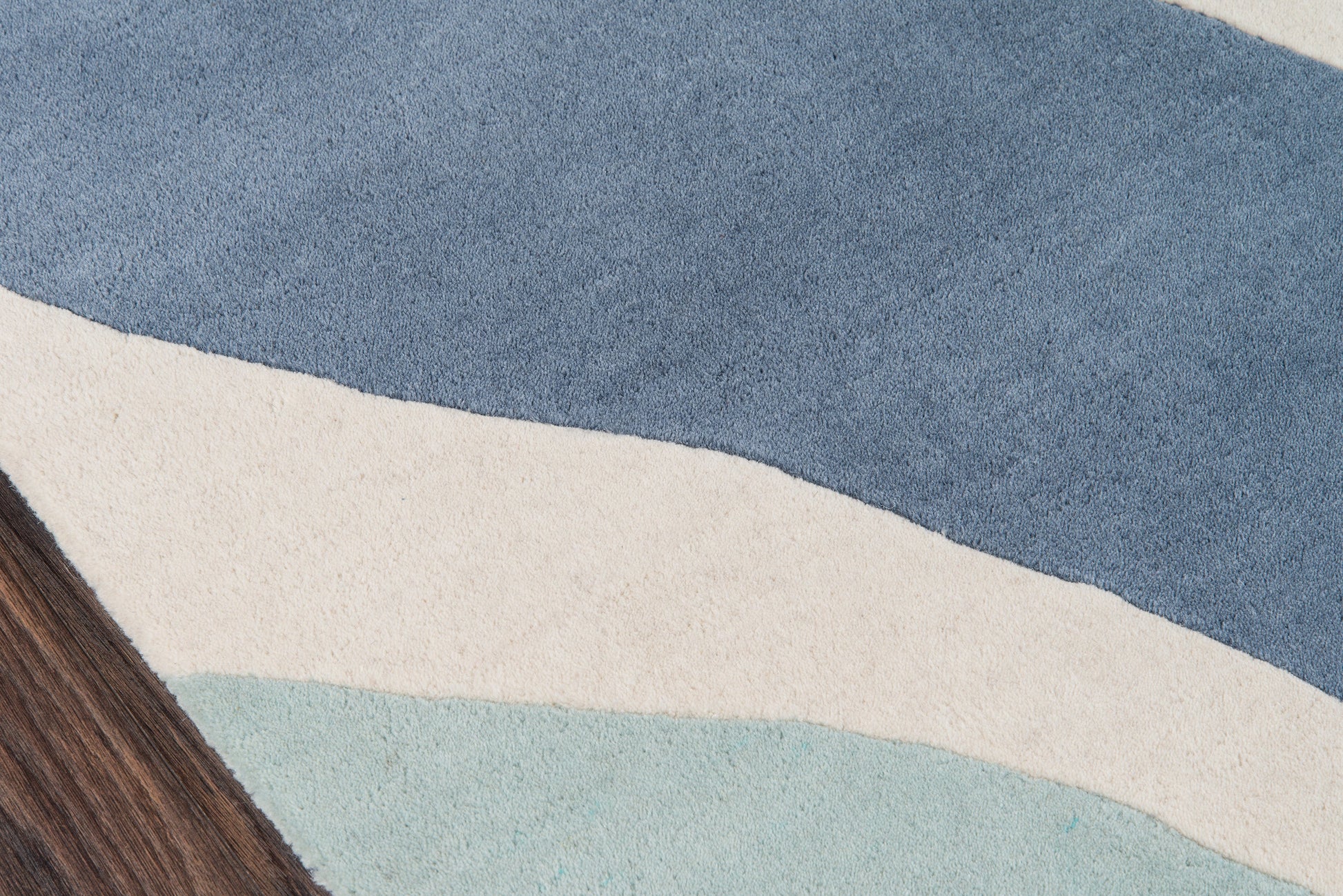 Abstract blue-toned rug with layered wave shapes in dark blue, cream, and pale teal; brown wood edge visible.