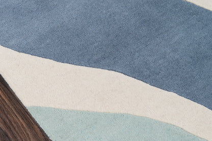 Abstract blue-toned rug with layered wave shapes in dark blue, cream, and pale teal; brown wood edge visible.