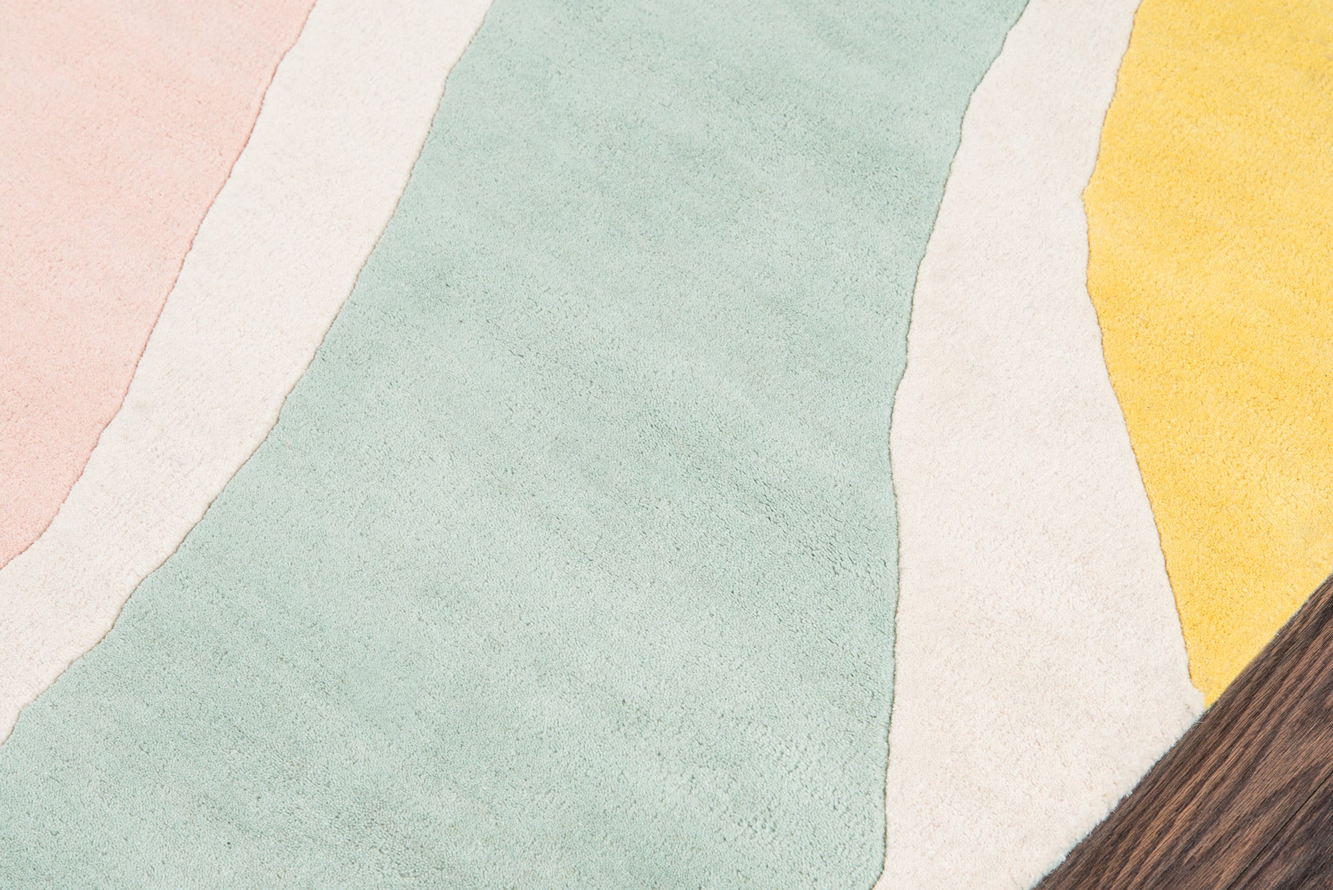Pastel striped rug with wavy bands in pink, mint, cream and yellow; soft textured textile with a wood edge.