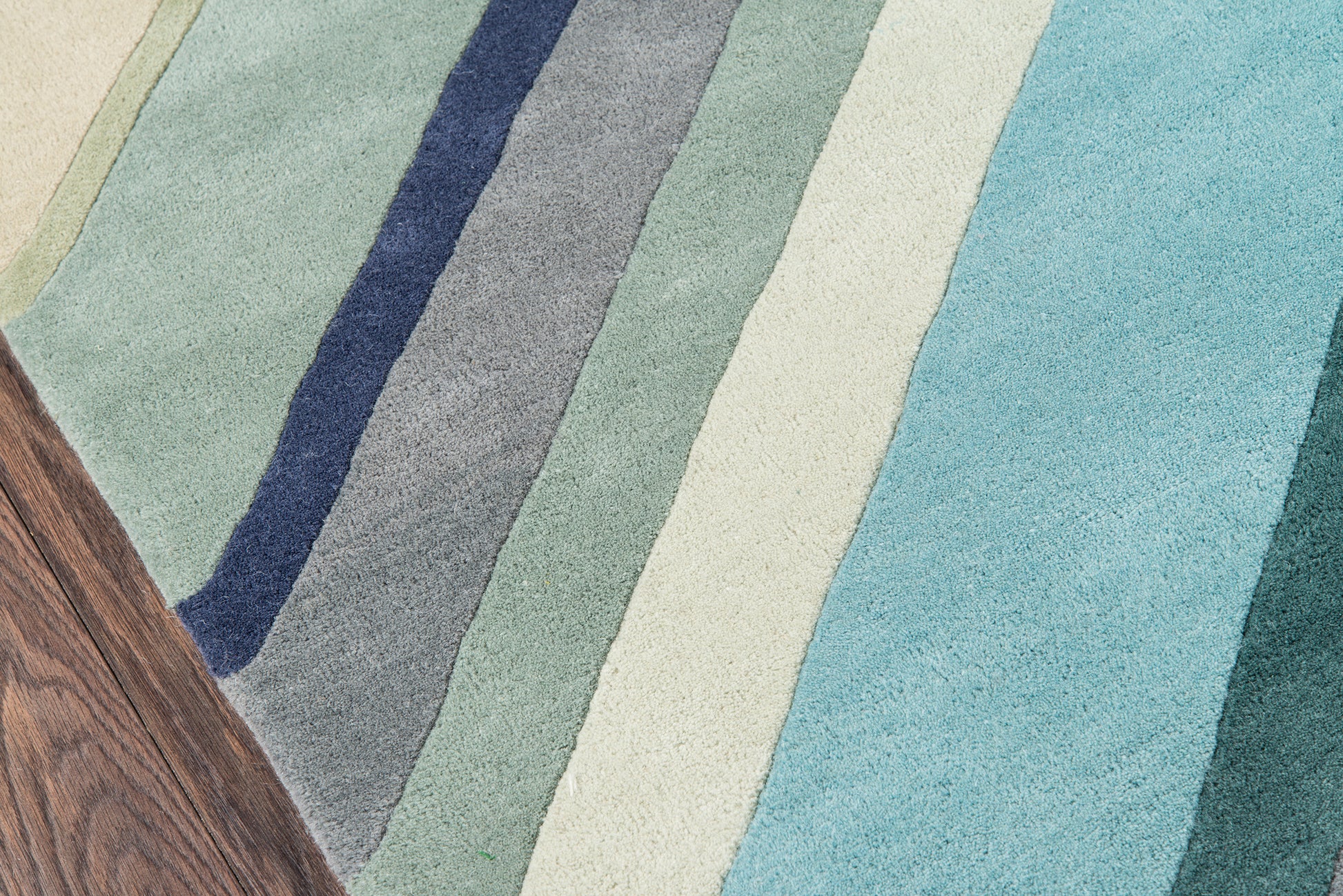 Soft woven 2' x 8' runner rug with diagonal stripes in blues, teals, mint greens & cream; wood-toned corner.