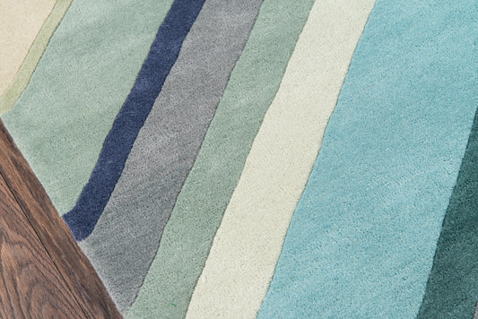 Pastel diagonal-striped rug in blues, teals, gray and cream tones; woven textile on wood floor.