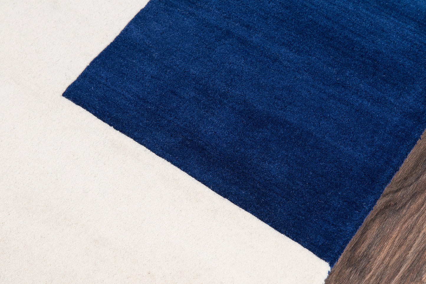 Deep blue plush rectangular rug on a light beige floor with a wooden plank edge.