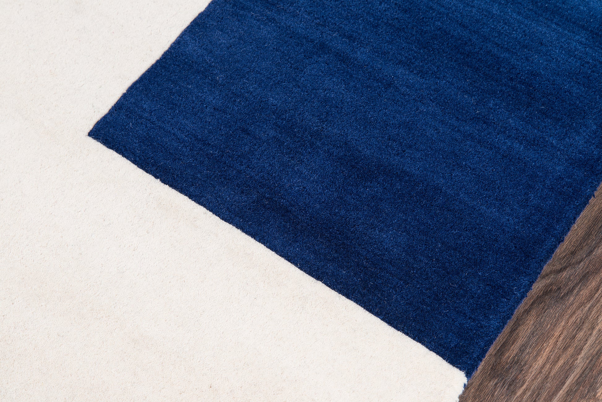 Royal blue rectangular rug on light beige floor with wood edge.