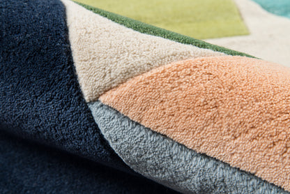 Close-up of a rolled multi-color patchwork rug with plush loop pile in navy, beige, peach and blue-gray.