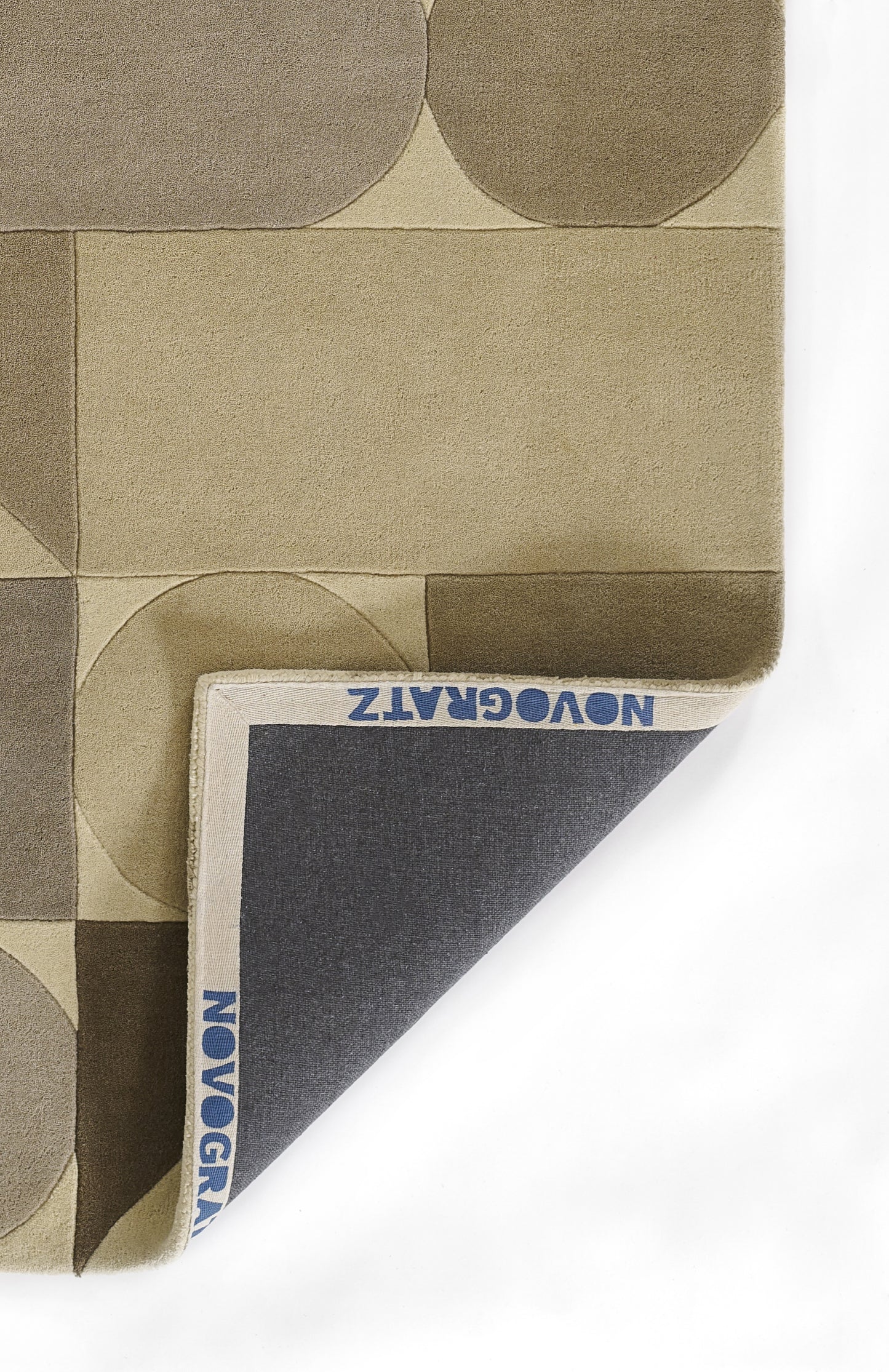 Geometric beige rug with taupe circles and rectangular blocks; folded corner reveals navy backing with brand text.