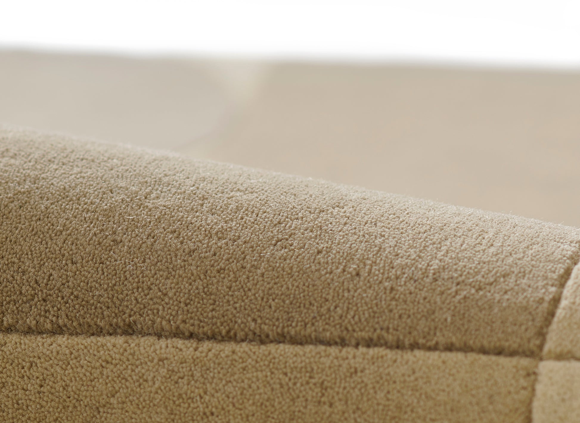 Beige microfiber suede upholstery close-up on a curved sofa edge with seam.