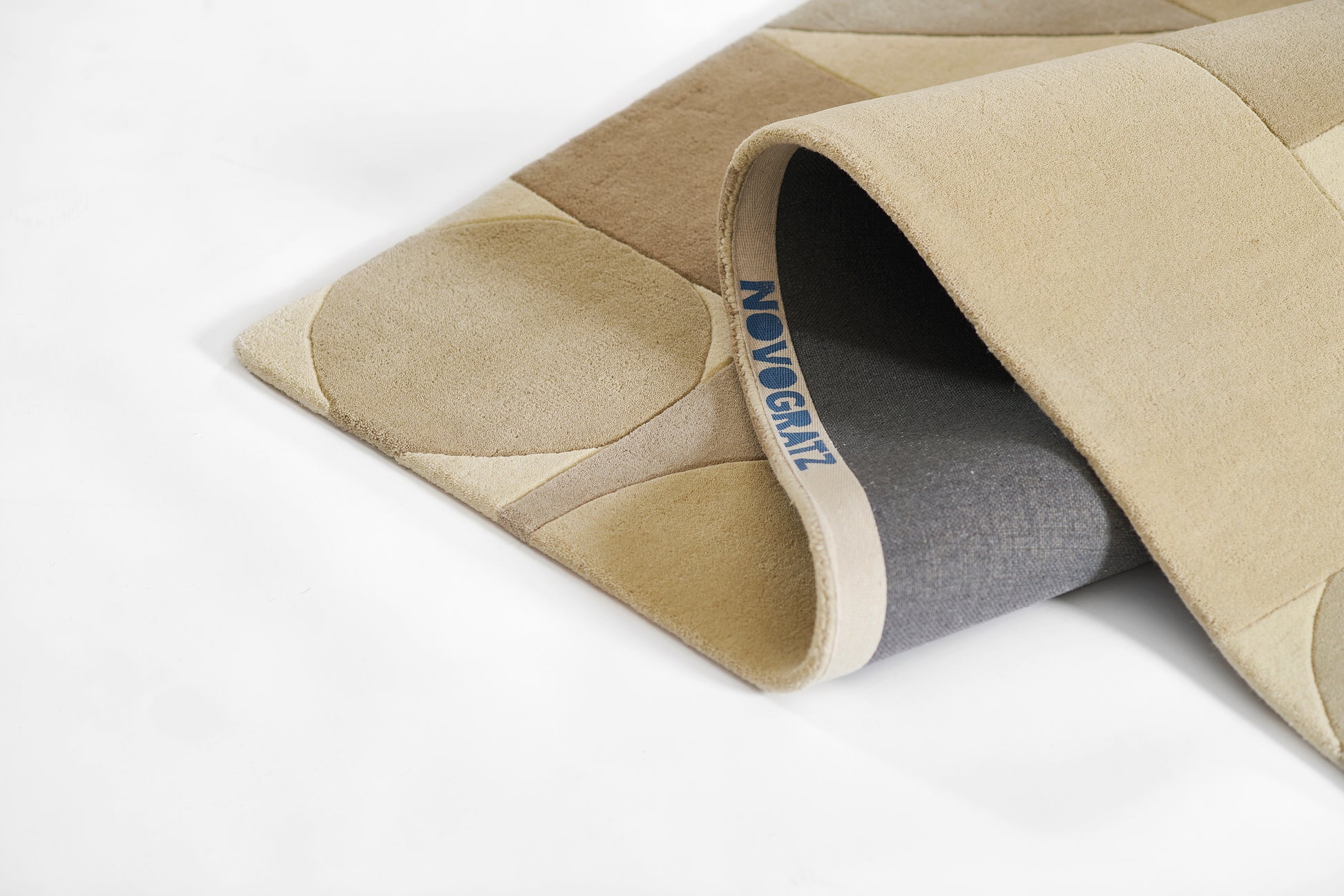 Beige quilted padded rug with stitched segments and rolled edge revealing gray underside.