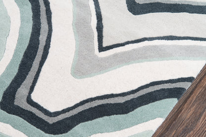 Abstract geometric rug with teal, blue-gray and black concentric lines; wooden table edge visible.