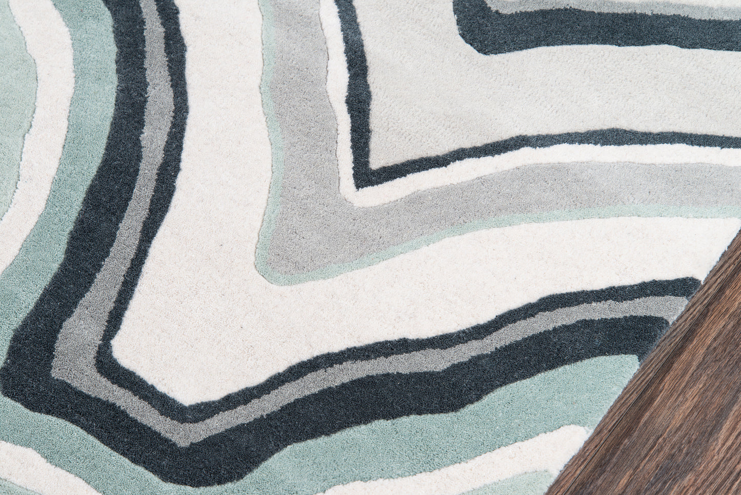 Abstract blue-green rug with bold black outlines in teal and navy on cream background; wooden table leg peeks in corner.
