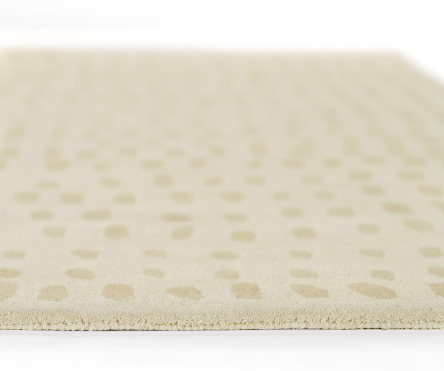 Beige rug with tan dotted pattern, soft plush pile and visible edge, close-up view.