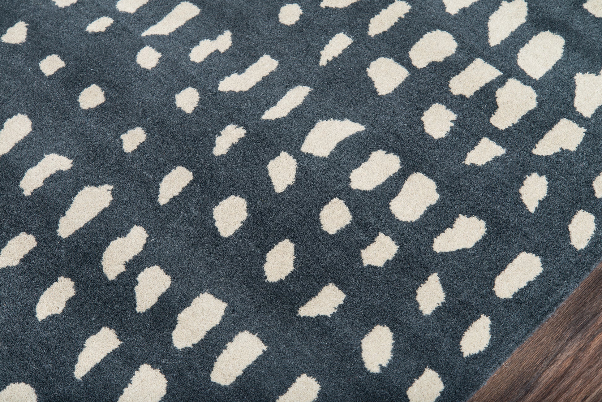 Navy blue area rug with irregular white dot pattern, modern abstract Dalmatian-inspired print, on a wooden floor.