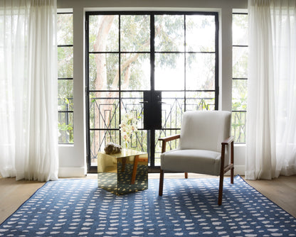 Bright living room with glass doors, sheer curtains, blue rug with white dots, cream armchair and gold cube table.
