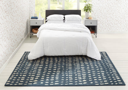 Blue rectangular area rug with cream oval motifs under a white quilted bedspread in a modern bedroom with two gray nightstands.