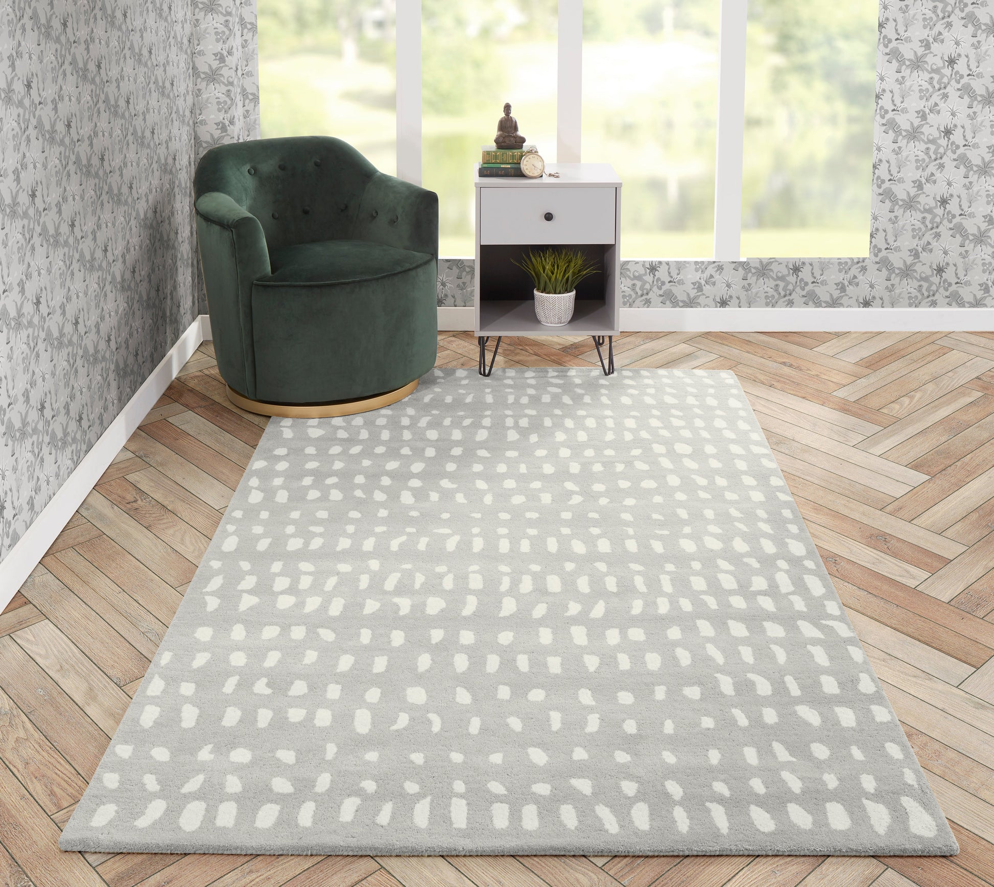 Gray patterned area rug with white dots on a wood floor beside a green velvet curved chair and a white side table with a plant.