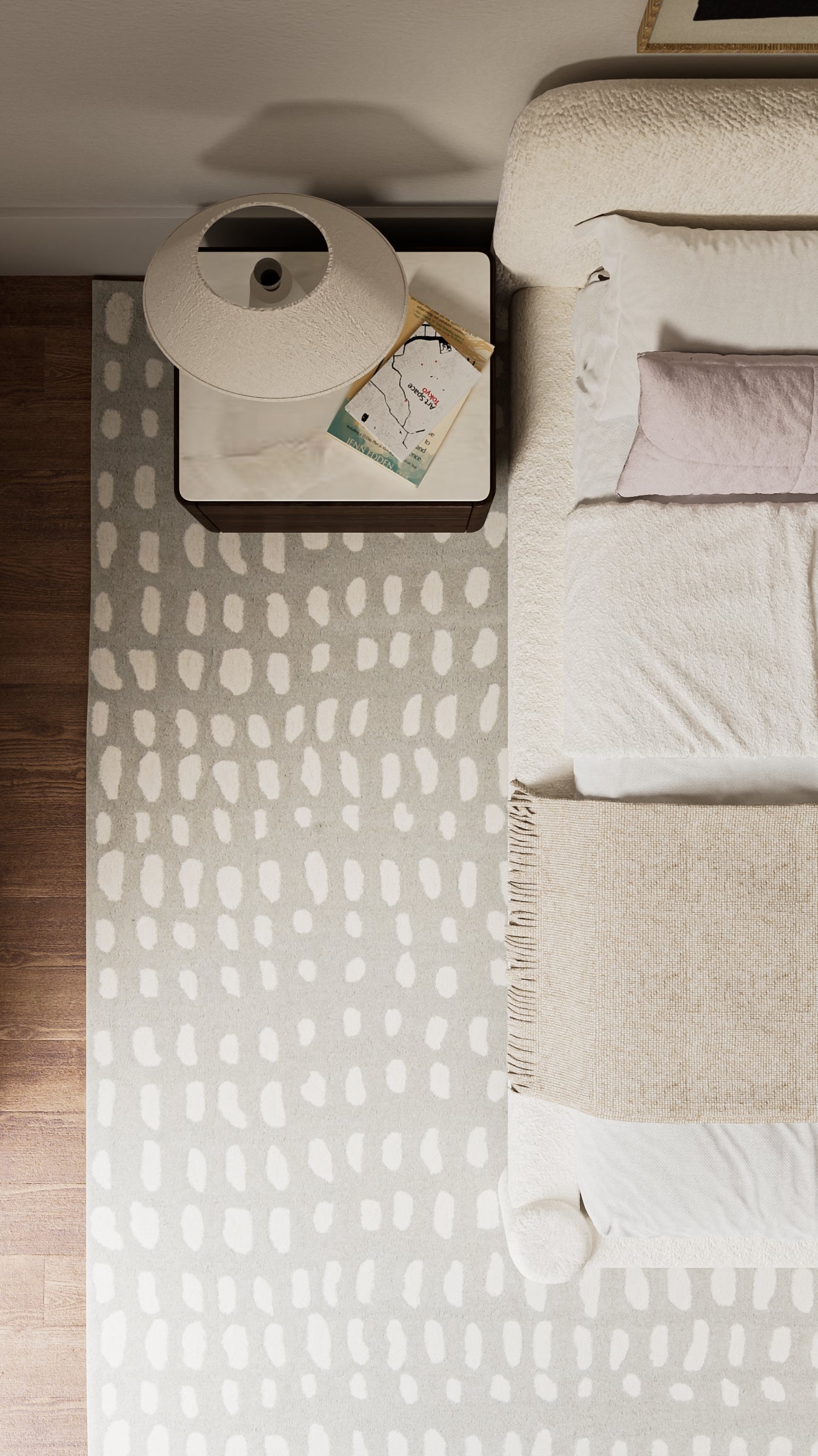Top-down view: grey patterned rug beside a white bed, beige throws, and a round white lamp on a dark wood nightstand.