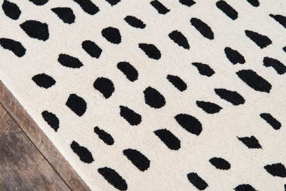 Ivory rug with irregular black Dalmatian-style spots on a wooden floor.