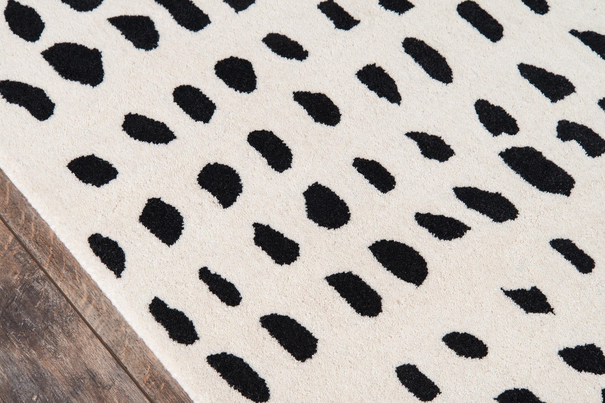 Ivory rug with black Dalmatian-spots pattern, rectangular, on a wooden floor.