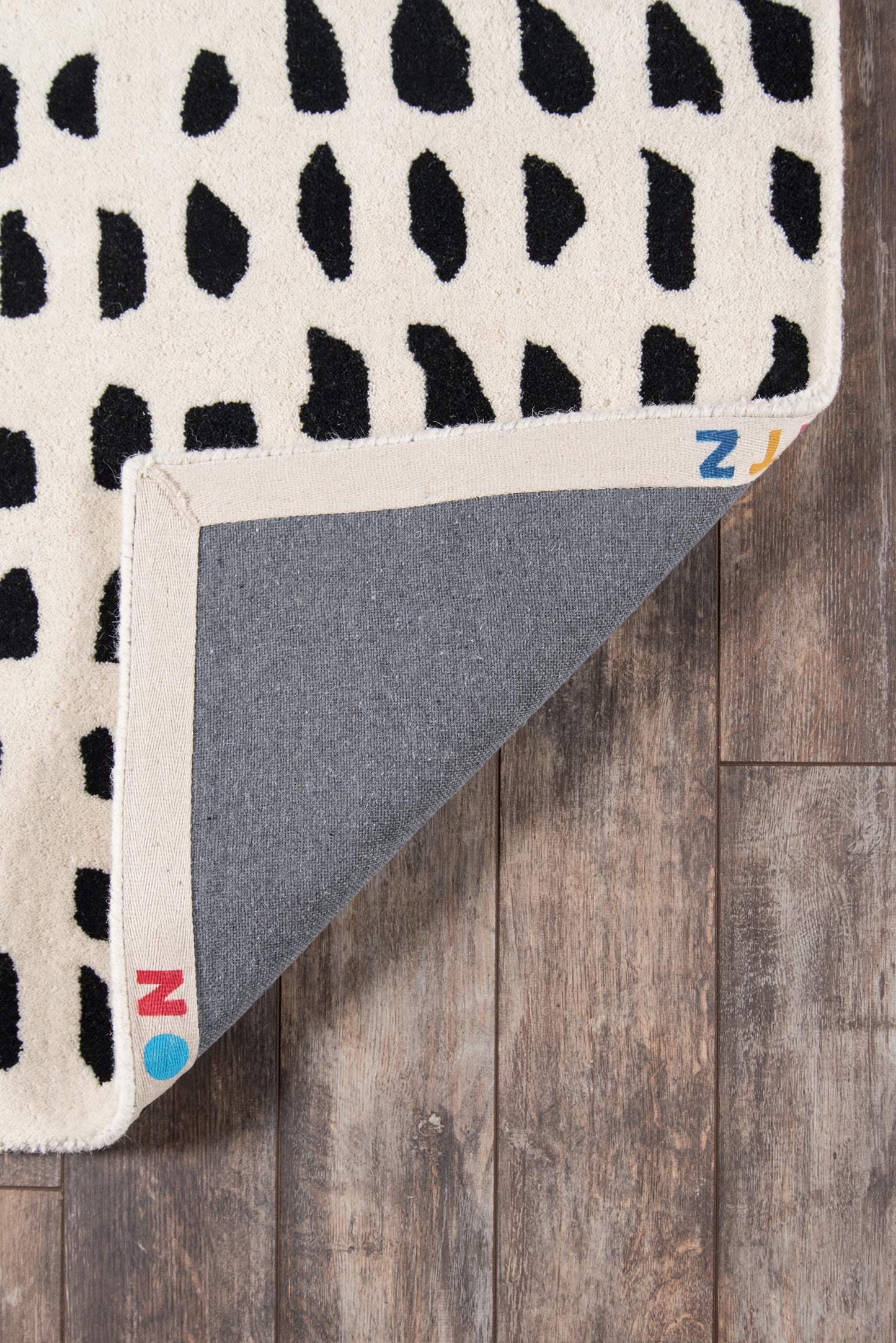 Ivory runner rug with irregular black spots; folded corner shows grey underside and beige border; modern decorative rug.