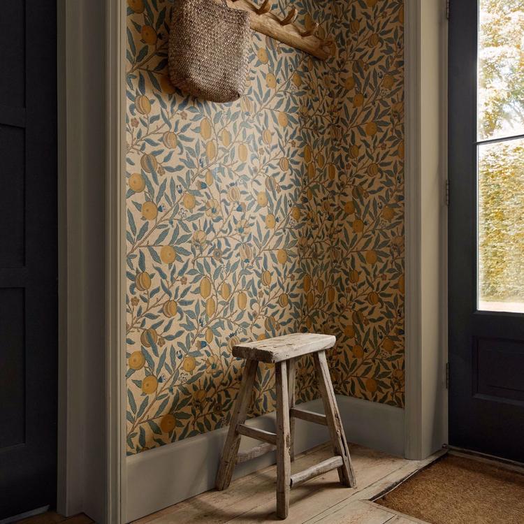 William Morris “Fruit” wallpaper in blue, gold, and brown tones showing detailed pomegranates and leaves in a classic Arts & Crafts pattern