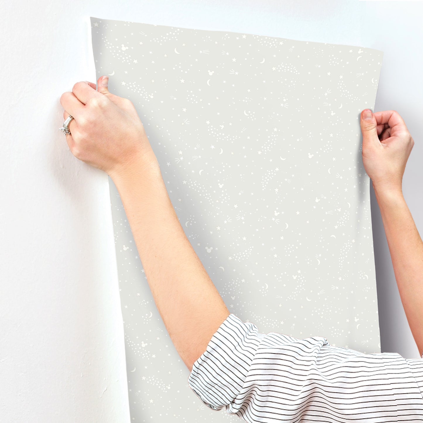 Hands hold a speckled light gray wallpaper sample with white stars for nursery decor