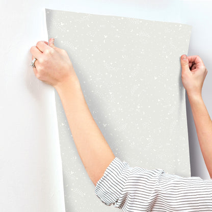 Hands hold a speckled light gray wallpaper sample with white stars for nursery decor