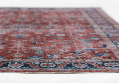 Persian-style red oriental rug with blue and ivory floral motifs, decorative border, wool texture, fringe edges.
