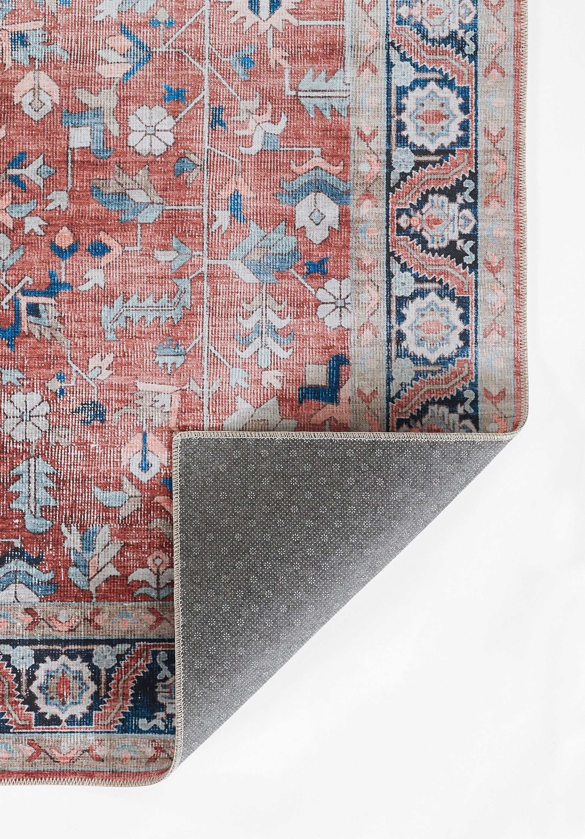 Persian-inspired pink rug with blue floral motifs and a navy geometric border; folded corner reveals grey dotted backing