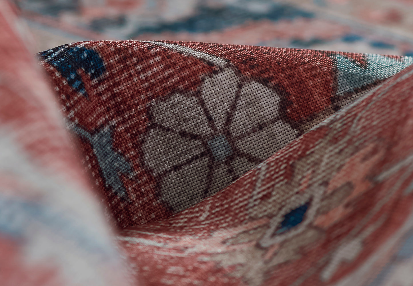 Close-up of red oriental rug fabric with blue and white floral-geometric patterns, woven wool texture.