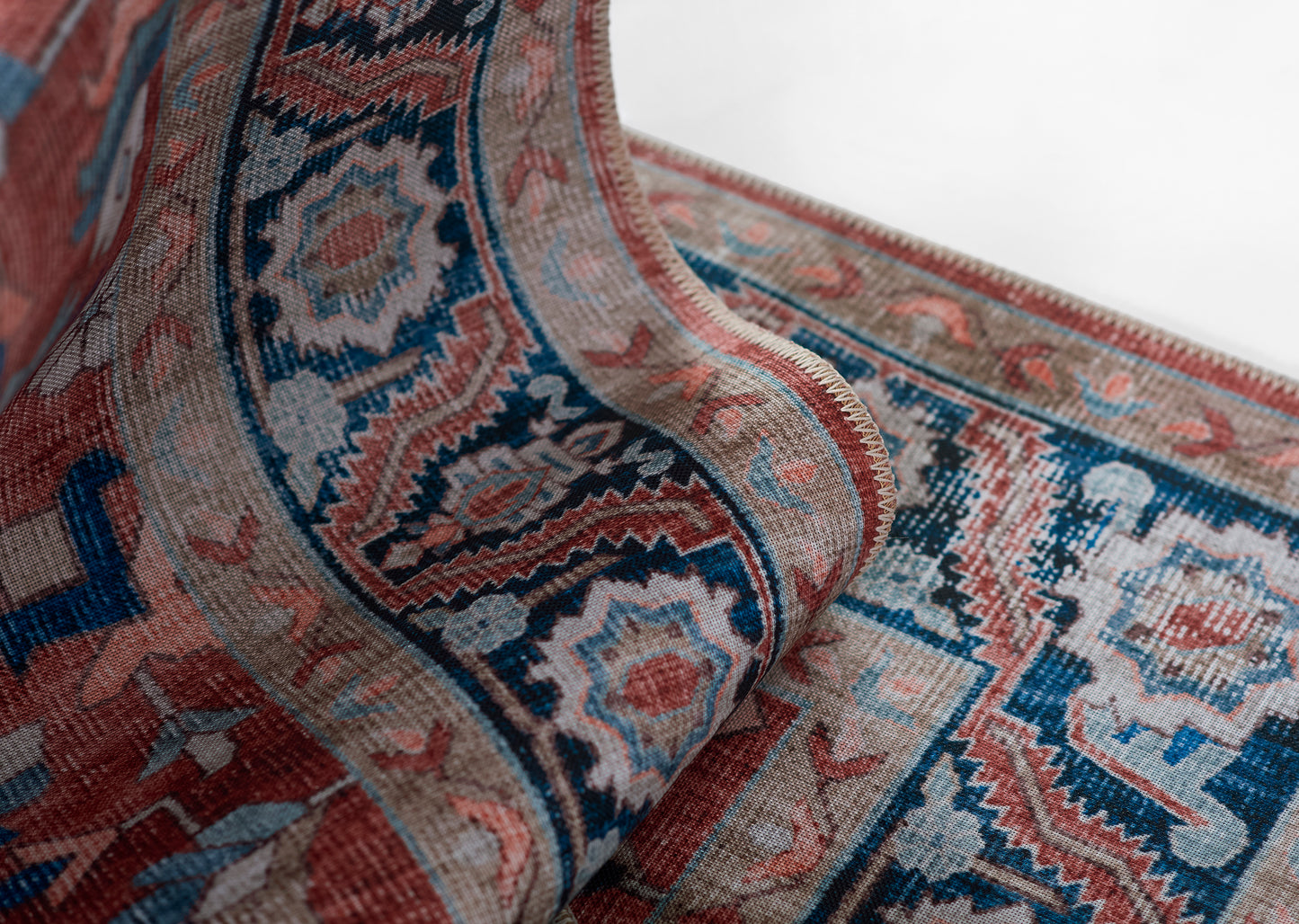 Close-up of an ornate rug with rolled edge, pink, blue, and cream geometric floral patterns.