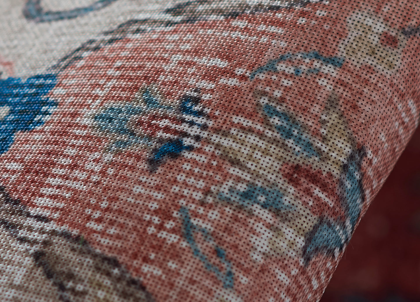 Close-up of a woven floral rug in red, blue and beige with visible texture and a curved folded edge.