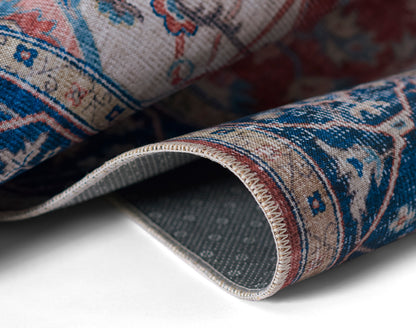 Close-up of rolled oriental rug in blue, beige and red with floral motifs and stitched edge.