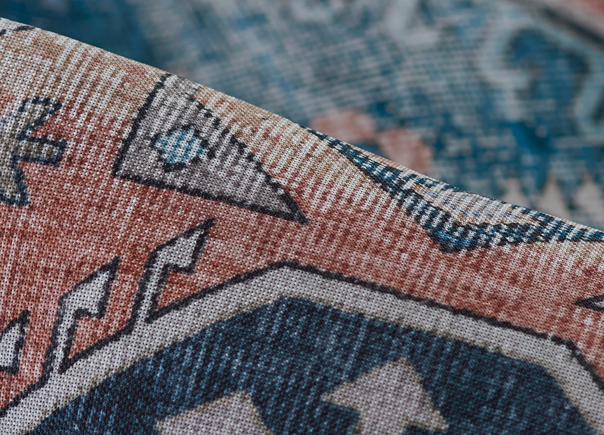 Close-up of a folded woven rug with blue, orange, and beige geometric tribal/kilim pattern.