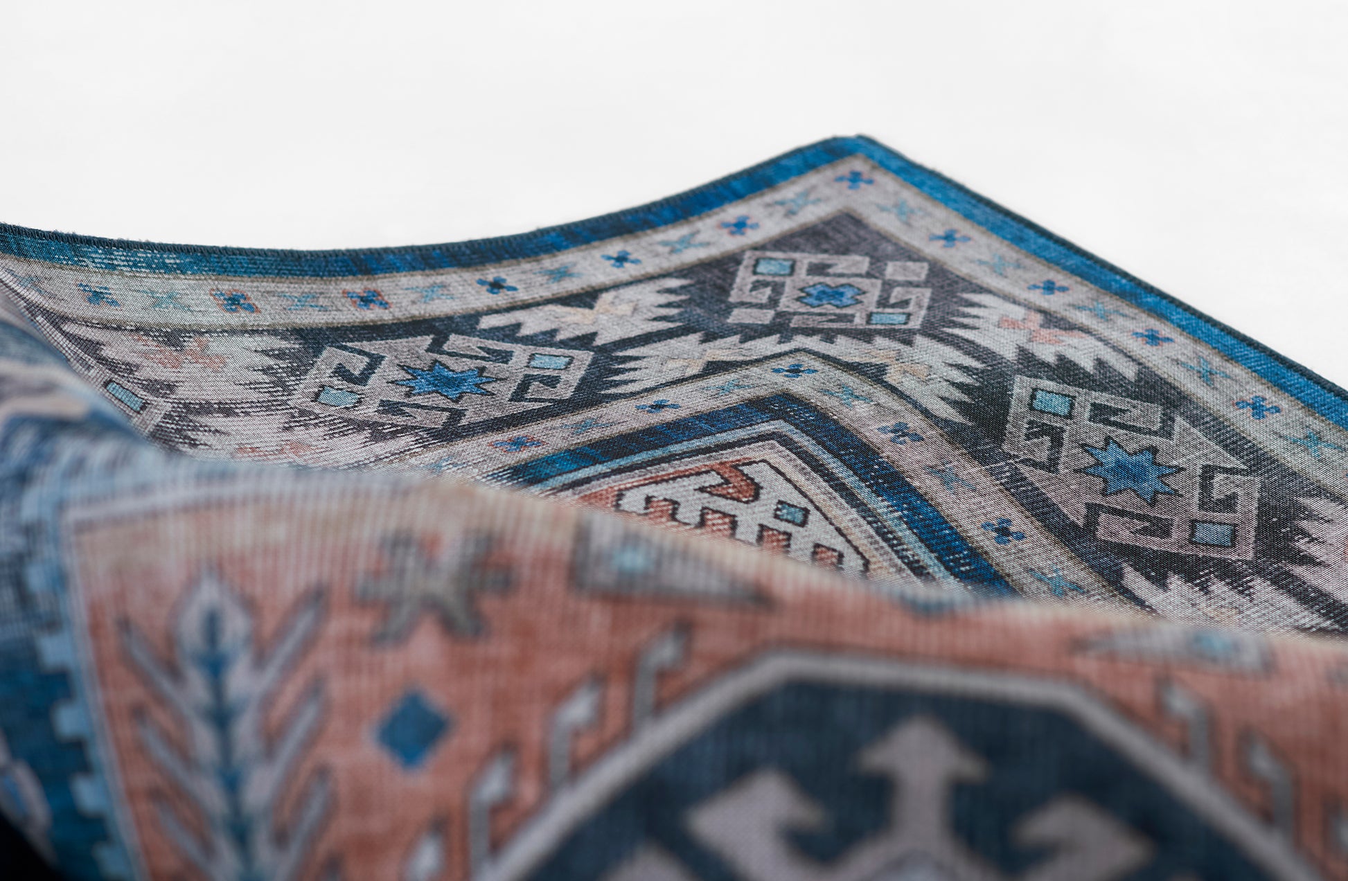 Blue-gray woven rug with diamond geometric patterns, folded to reveal a teal border and terracotta accents.