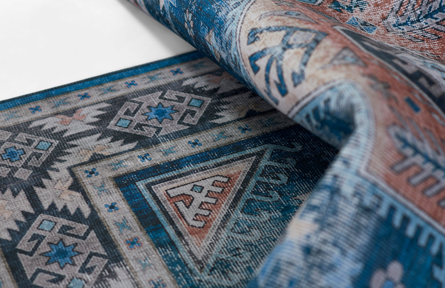 Rolled blue geometric rug with diamond and triangle motifs in teal, gray, and ivory; woven home decor textile.