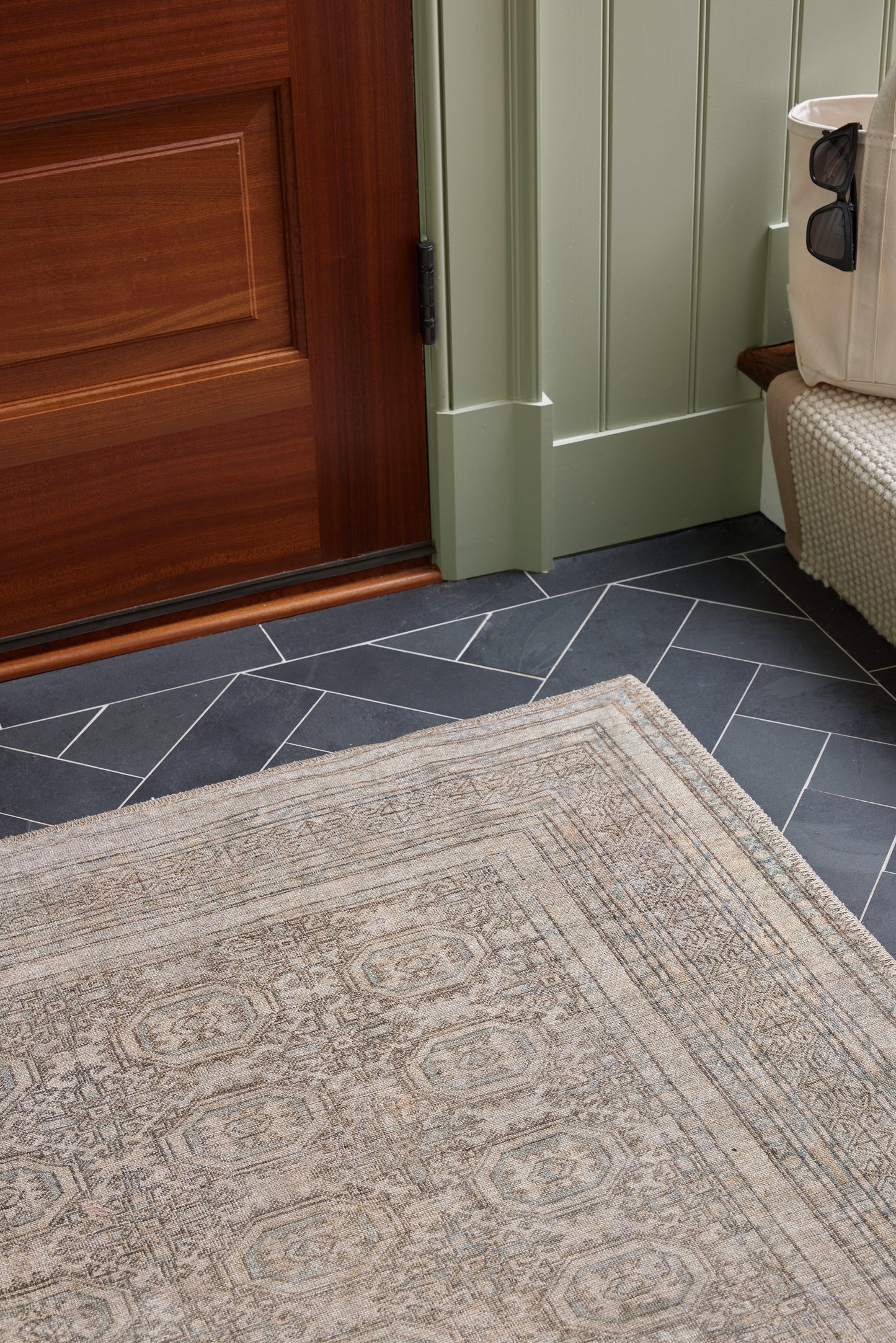 Beige patterned area rug on dark blue-gray tile floor near a wooden door and green paneled wall.
